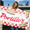 Person holding a Portillo's beach towel with hot dog graphics and picnic-check pattern.